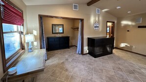 A spacious room with a large window, a wooden table with a lamp, a black dresser, and a ceiling fan. - Studio style guest house with Pool! (Georgetown)