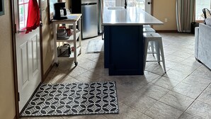A kitchen with a central island, a refrigerator, and a microwave. There is a door with a red curtain, a window with curtains, and a clock on the wall. - Studio style guest house with Pool! (Georgetown)