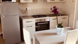 Une cuisine moderne équipée d’un réfrigérateur, d’un four à micro-ondes, d’une cuisinière, d’un four et de meubles blancs. On y trouve une table à manger avec des chaises et une orchidée en pot.