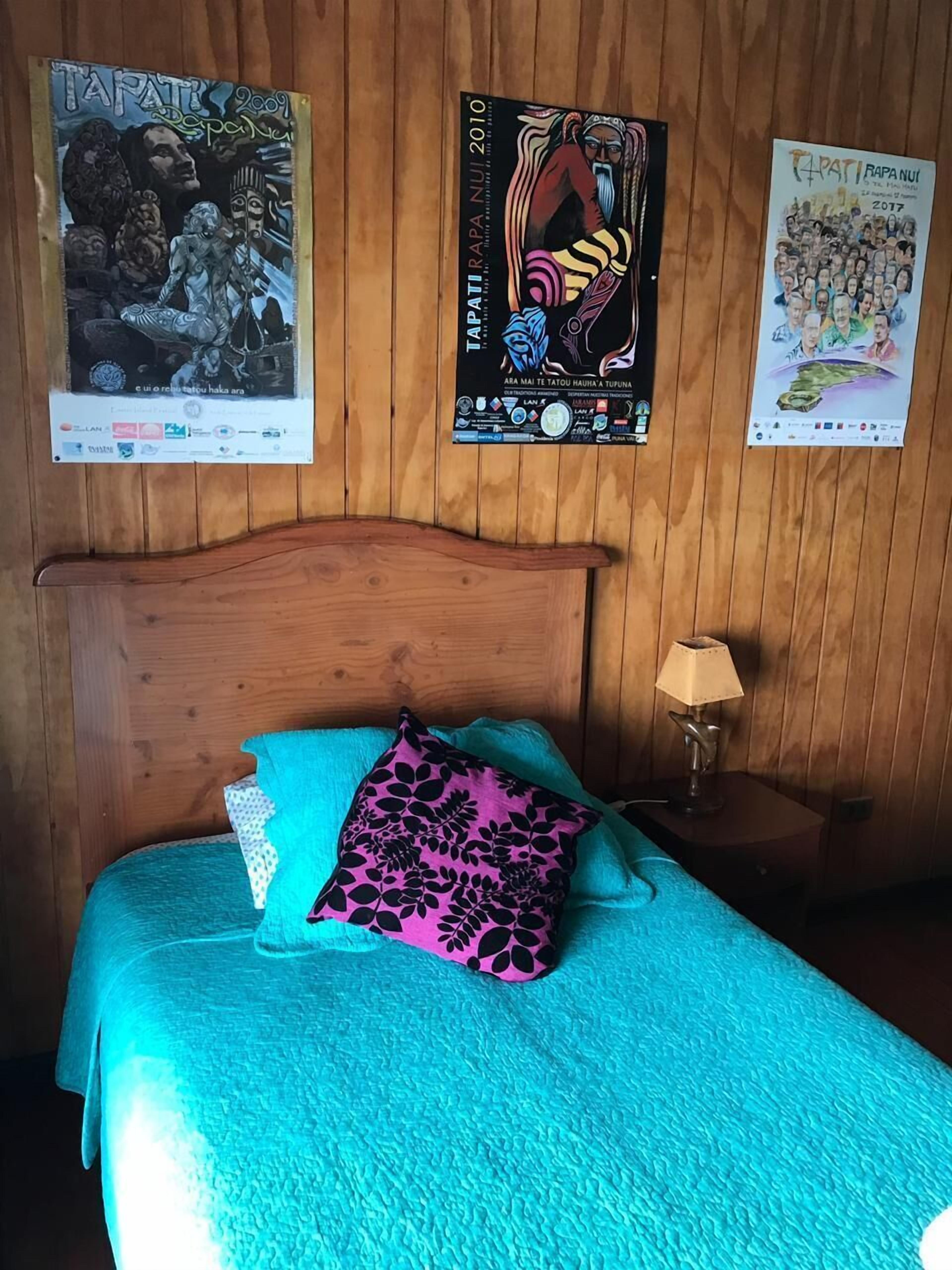 A room with a wooden headboard, a bed with teal bedding and a pink patterned pillow, and posters on the wall.