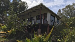 A two-story house with a balcony, surrounded by lush greenery and trees. - Cabañas Mana Ora (Hanga Roa)