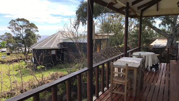A wooden deck with a railing, tables, and chairs. - Cabañas Mana Ora (Hanga Roa)