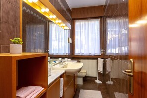 A modern bathroom with a vanity, sink, and toilet. There is a potted plant on the vanity, and the room has a large mirror with lights above it. - Villa Mary with garden (Arco)