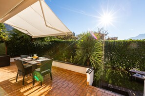 An outdoor patio with a table and chairs, a white canopy, and a view of a mountain and greenery. - Villa Mary with garden (Arco)