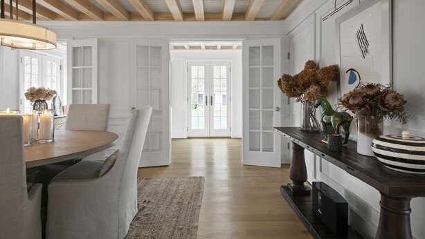 A spacious room with a wooden ceiling, a dining area with a table and chairs, and a console table with decorative items.