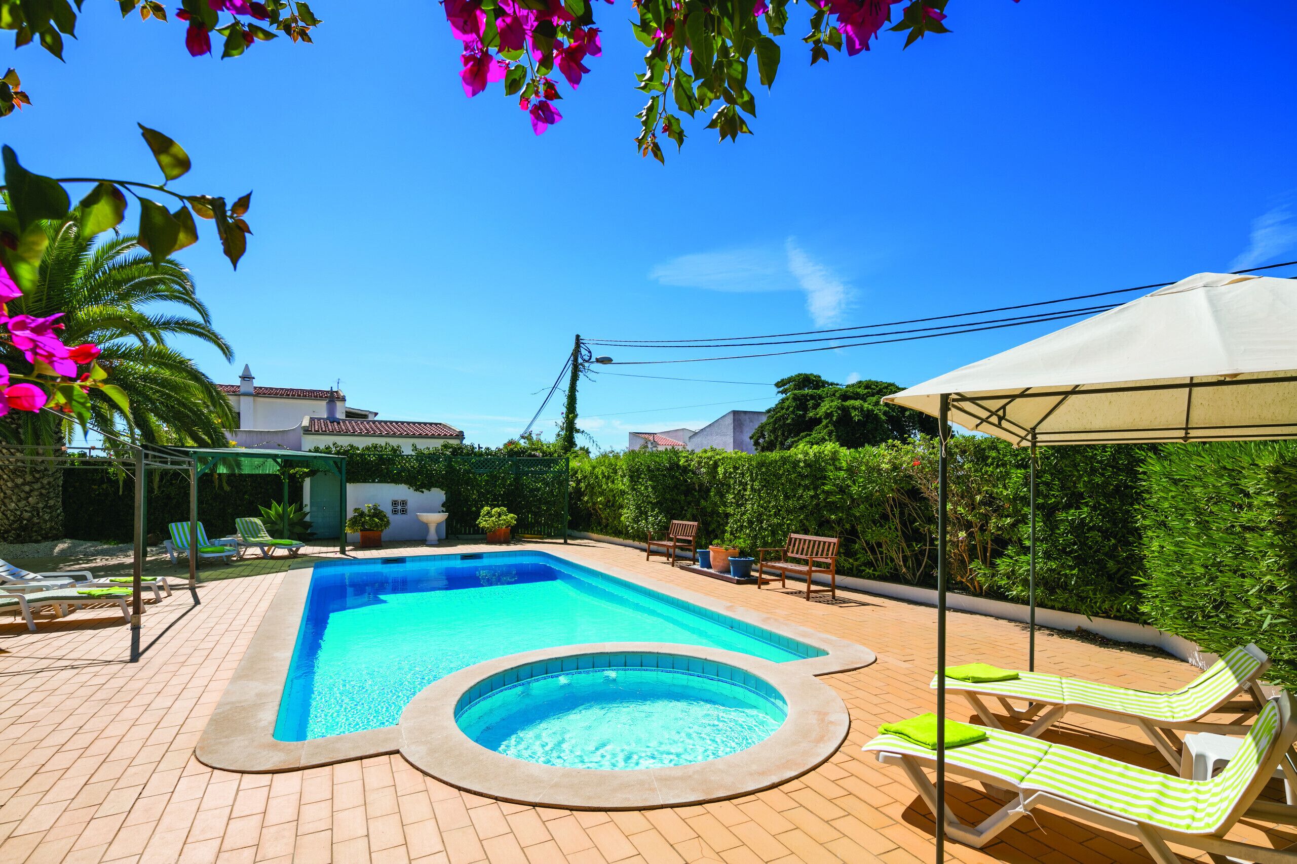 A rectangular swimming pool with a hot tub, surrounded by lounge chairs and a covered area.