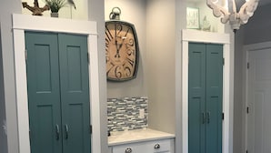 Una cocina con puertas dobles color turquesa, un reloj de pared grande, un salpicadero de azulejos y una isla blanca con un lavamanos.