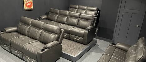 A home theater with a large reclining sofa and a smaller sofa, both in a dark room with a door and a wall-mounted decoration.