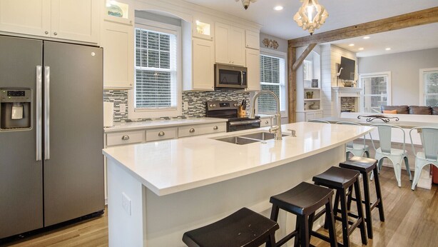 Una cocina moderna con armarios blancos, un refrigerador de acero inoxidable, una isla grande con taburetes de bar y una viga de techo de madera.