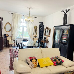 Un salon comprenant un canapé, une table à manger, des chaises, un lustre, une bibliothèque et un miroir.