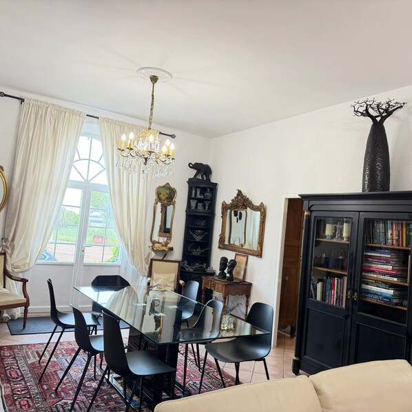 Un coin repas avec une table en verre, des chaises noires, un lustre et une bibliothèque remplie de livres.