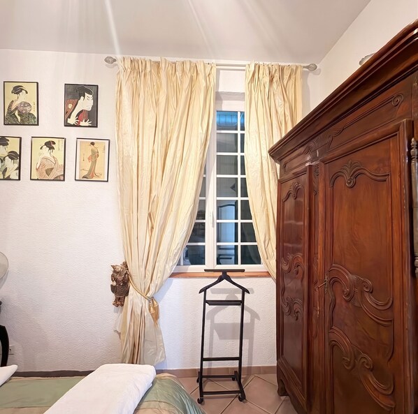 Ein Schlafzimmer mit einem Bett, einem Holzschrank, einem Fenster mit Vorhängen und Wandbildern.