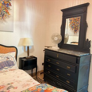 Un dormitorio con cama, cómoda, espejo, lámpara y un adorno en la pared.