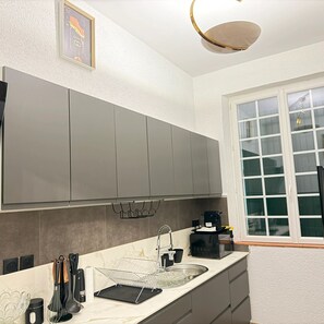 Une cuisine moderne avec des meubles gris, un plan de travail en marbre, une machine à café et une fenêtre avec des stores.