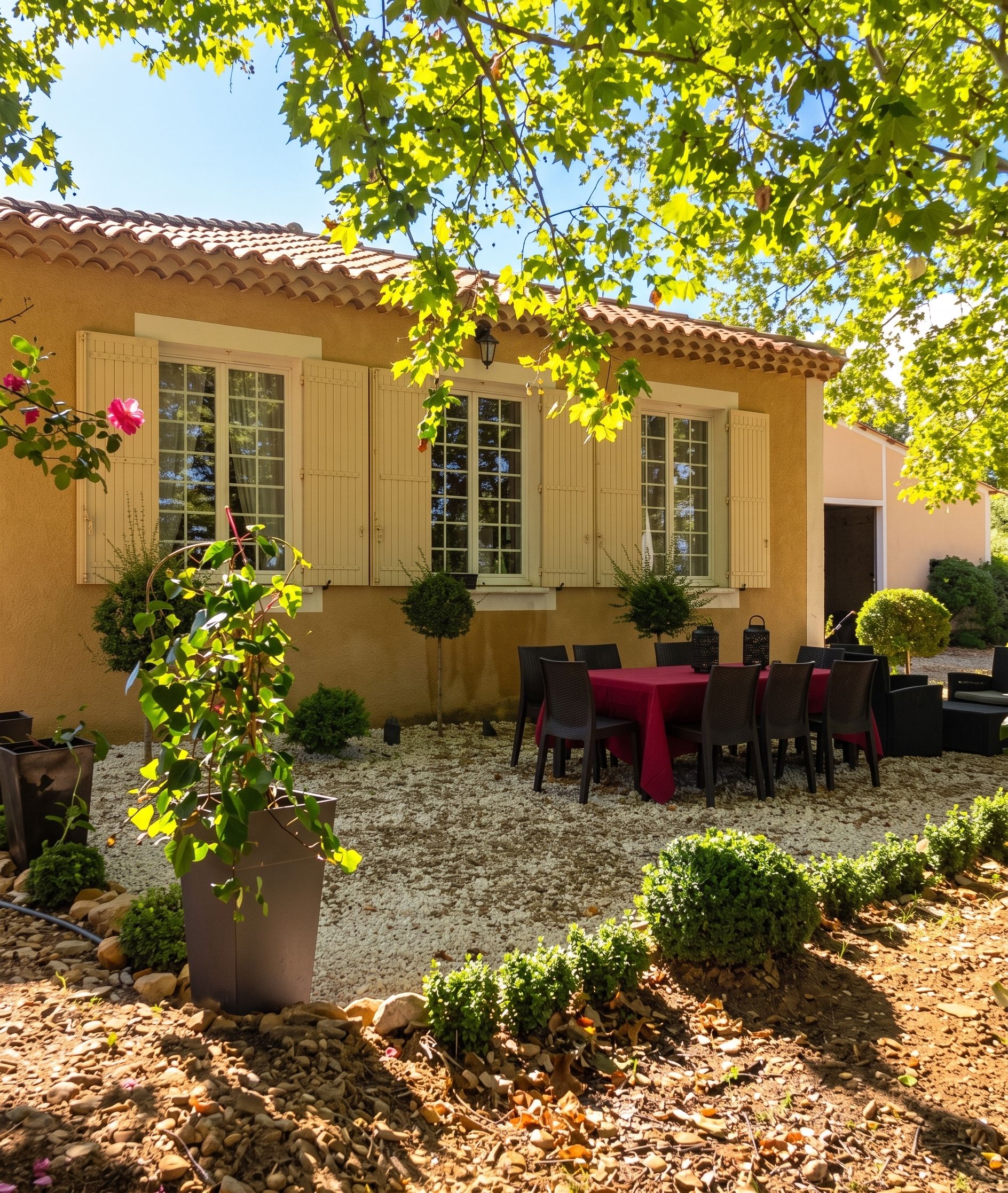 Un bâtiment avec un toit en tuiles, une terrasse avec une table et des chaises, et des plantes en pot.