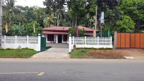 A gated entrance to a building with a red roof, surrounded by lush greenery and a white picket fence. - Hotel  Jonkoping (Godakawela)