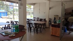 A dining area with tables and chairs, a refrigerator, and a counter with a person in the background. - Hotel  Jonkoping (Godakawela)