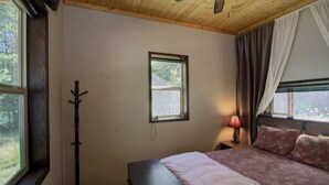 Een slaapkamer met een bed, een raam, een kapstok en een lamp.