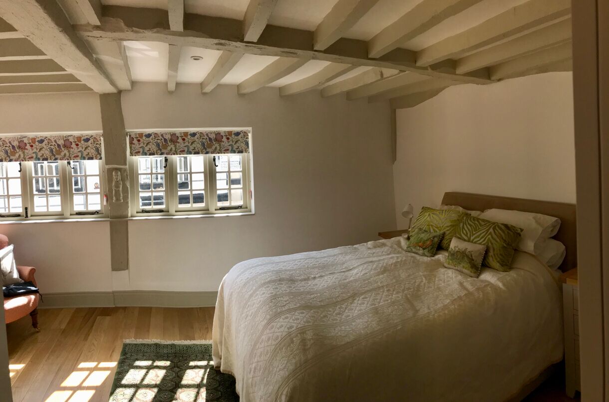 Quarto com uma cama grande, janela com cortinas florais e piso de madeira.