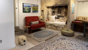A cozy living room with a stone fireplace, a red sofa, and a fluffy white dog.