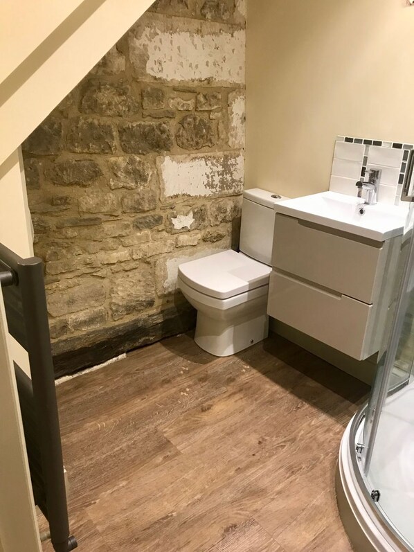Un baño compacto con pared de piedra, inodoro blanco y lavamanos pequeño.