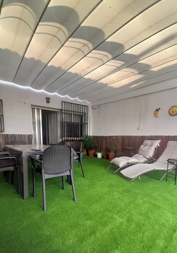 Un espace extérieur abrité comprenant une table et des chaises, un fauteuil et des plantes en pot.