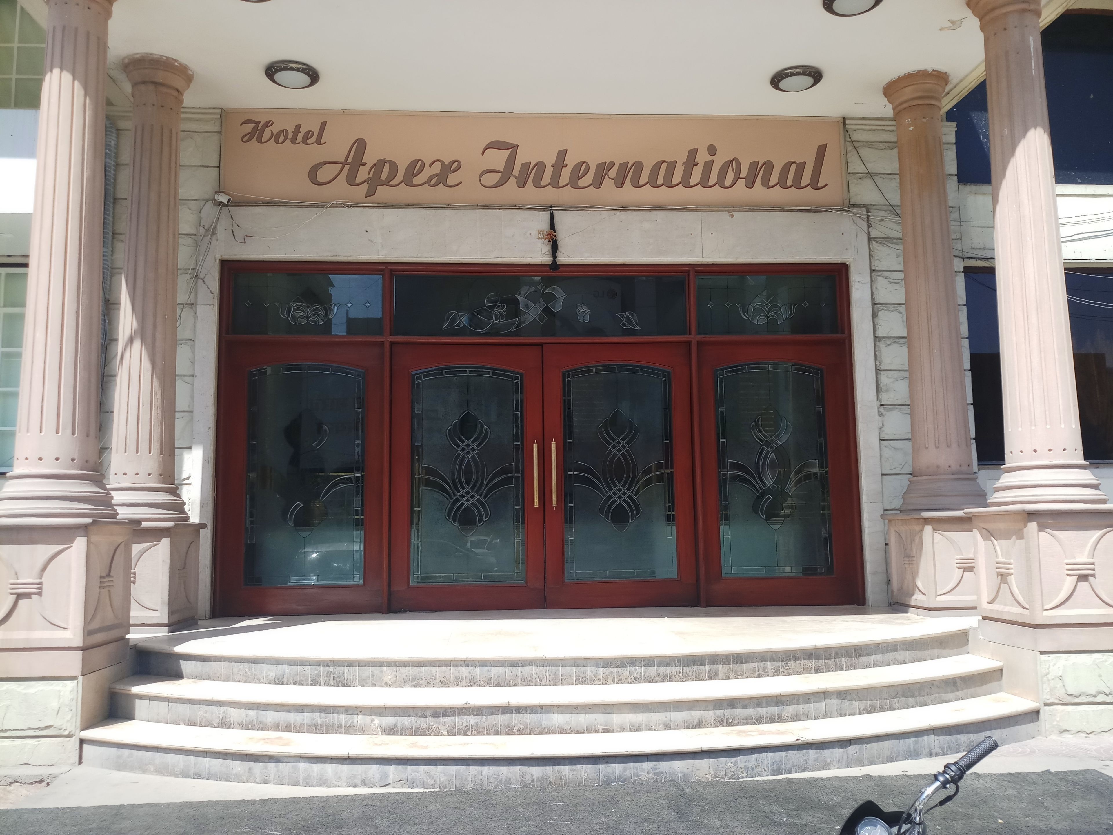 The entrance of Hotel Apex International with a sign above the doors, large glass windows, and a set of steps leading up to the entrance.