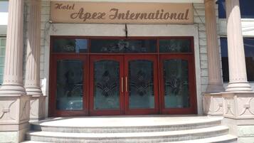 The entrance of Hotel Apex International with a sign above the doors, large glass windows, and a set of steps leading up to the entrance.