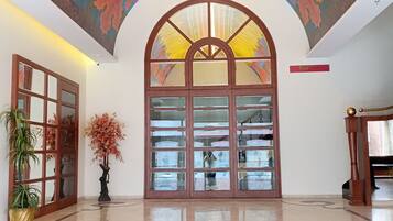 A lobby with a large arched doorway, a ceiling mural, and a polished floor.