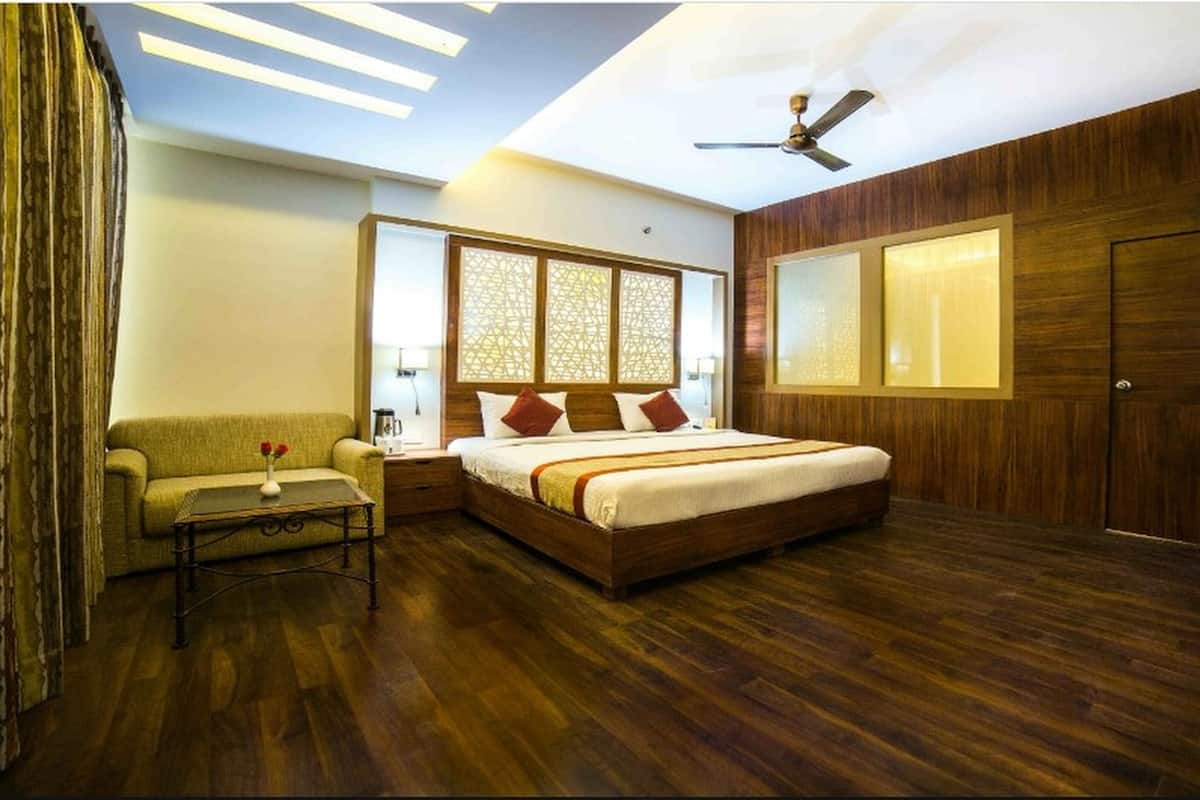 A bedroom with a large bed, a sofa, a small table with flowers, a ceiling fan, and wooden paneling.