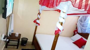 Una cama individual con dosel, un televisor montado en la pared, una mesita con una cesta y un cubo de basura.