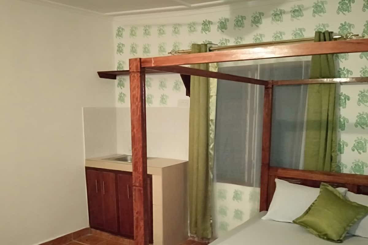 Ein Zimmer mit einem hölzernen Himmelbett, einem kleinen Schreibtisch und einem Schrank.
