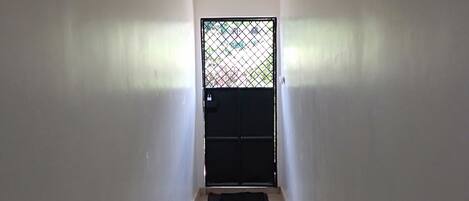 Un pasillo estrecho con suelo de baldosas que conduce a una puerta negra con reja de metal.