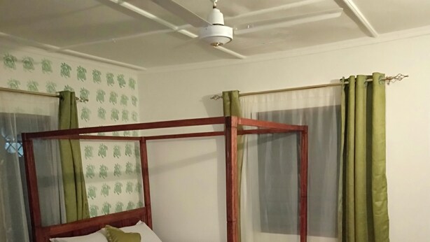 A four-poster bed with a wooden frame and a canopy, a green bedspread, and a pillow. - Mali Guest House (Mombasa)
