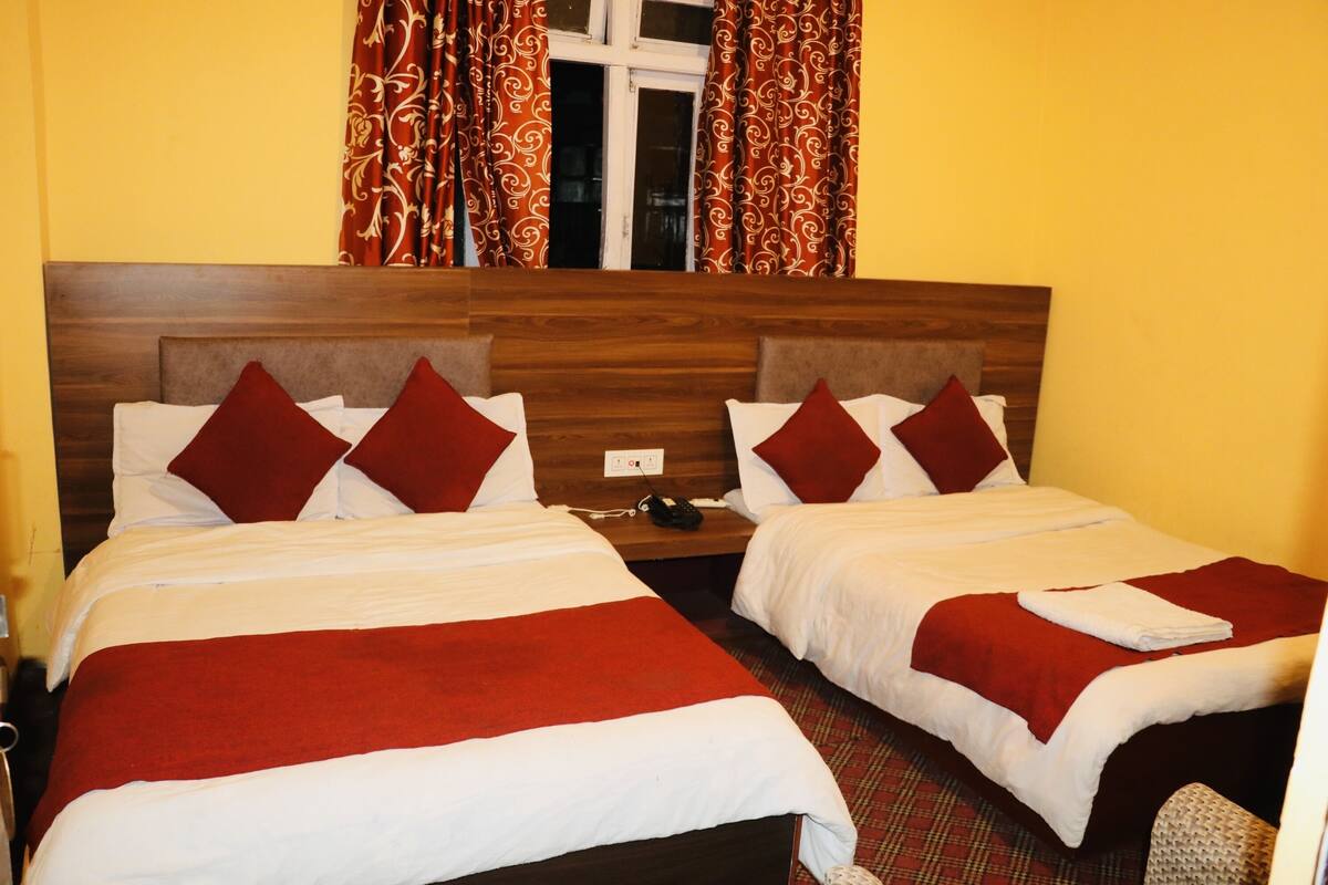 Habitación doble con dos camas, cada una con ropa de cama roja y blanca, cabeceros de madera y una ventana con cortinas estampadas.
