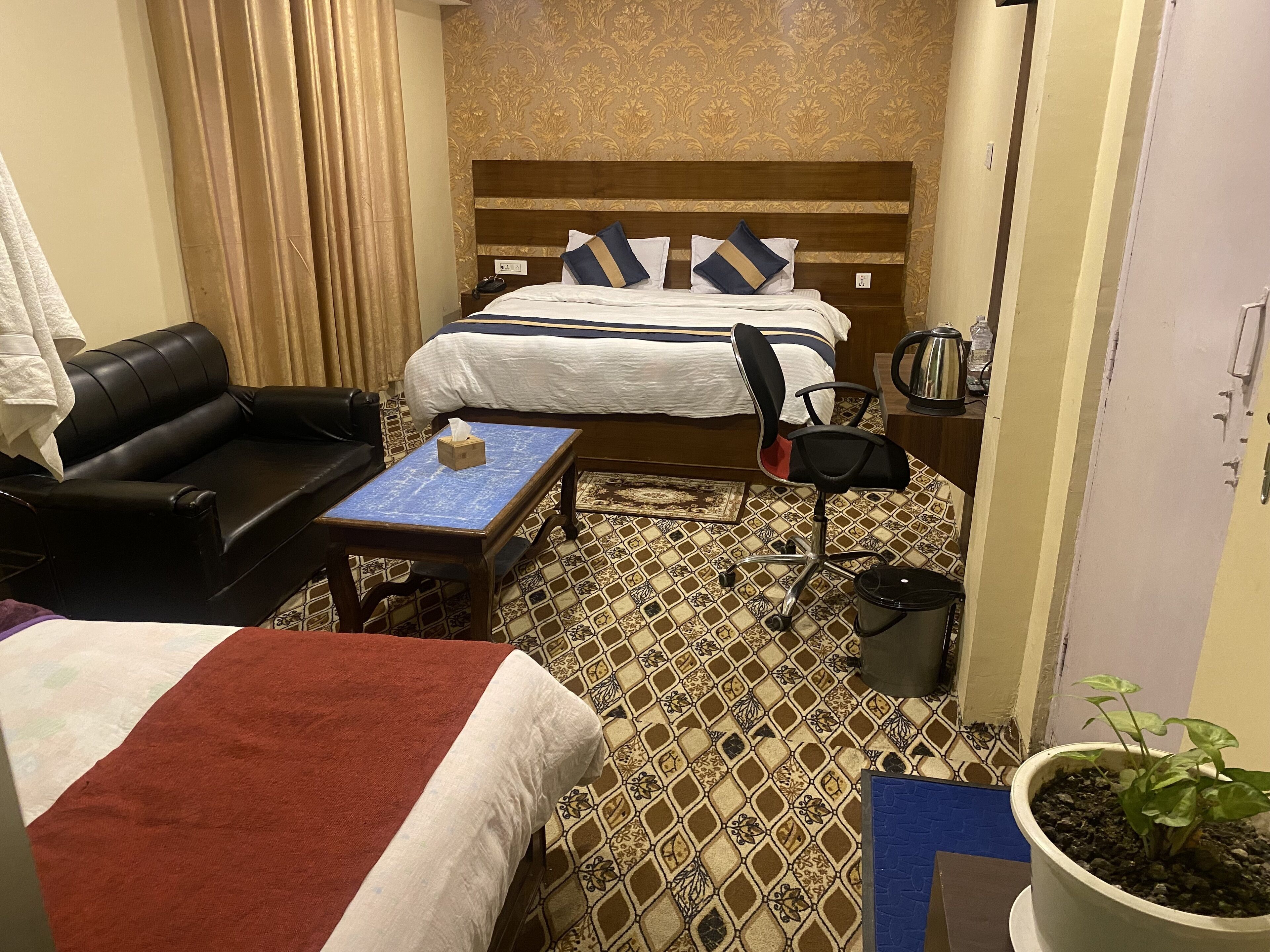 A hotel room with two beds, a sofa, a small table, a chair, a potted plant, and a coffee maker.