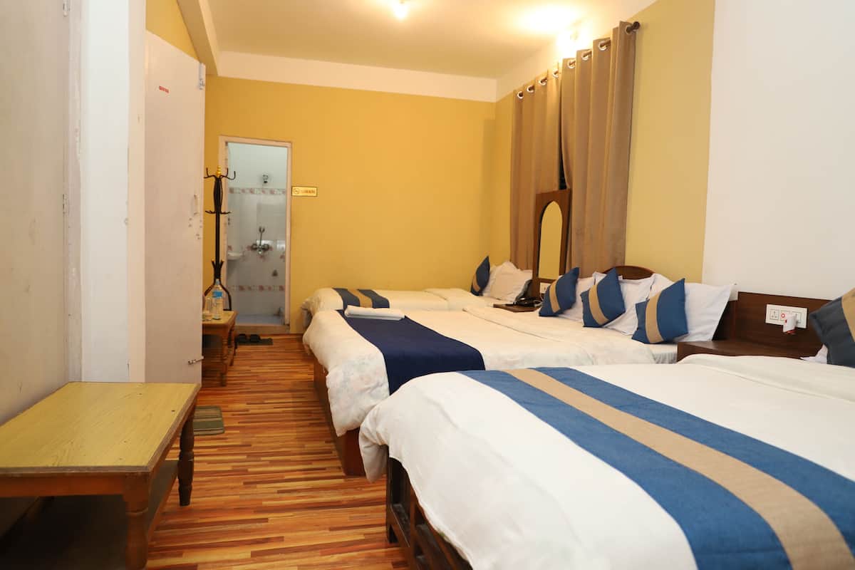 Habitación de hotel con tres camas, piso de madera, una mesita y baño visible a través de una puerta abierta.