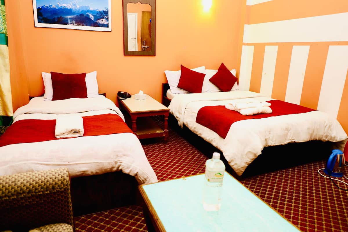 Habitación de hotel con dos camas, cada una con ropa de cama roja y blanca, una mesita con una botella y una silla.