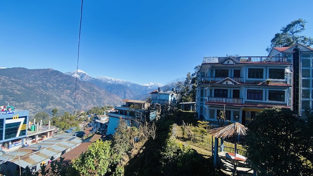 A multi-story building with a balcony, surrounded by greenery and mountains in the background. - Taplejung Hotel Pathivara (Taplejung)
