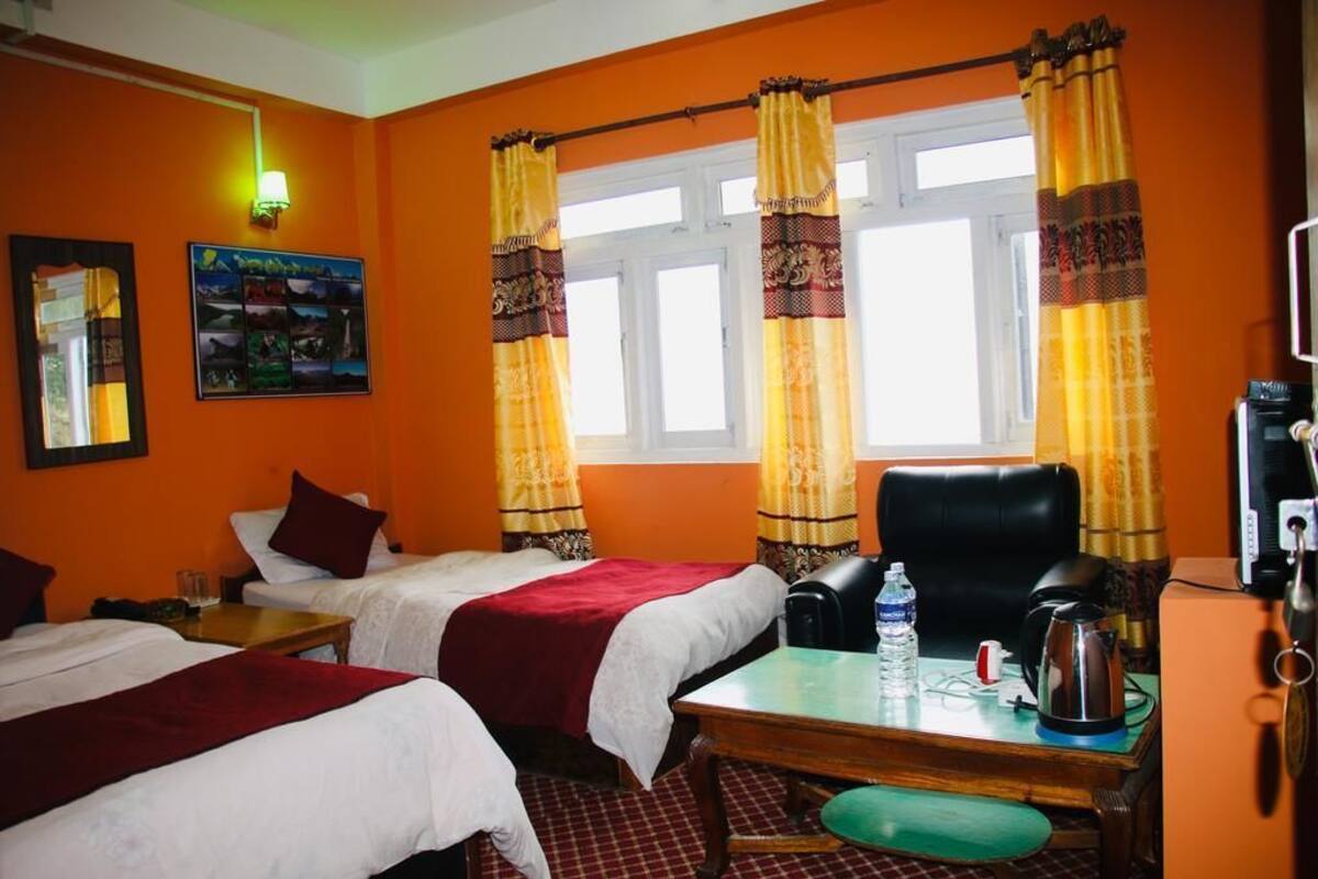 Habitación de hotel con dos camas, un escritorio con hervidor, una silla y cortinas.