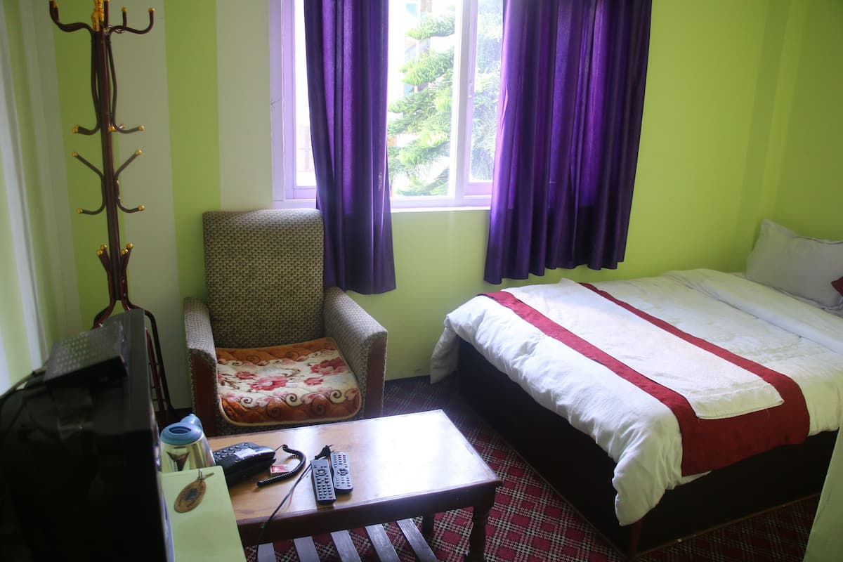 Habitación de hotel con cama, una silla, escritorio con computadora y controles remotos, y ventana con cortinas.