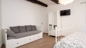 Ein Schlafzimmer mit einem weißen Sofa, einem Bett mit floralem Überwurf, einem Kleiderschrank und einem an der Wand befestigten Fernseher.