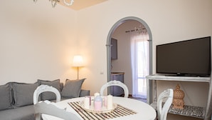 A cozy living room with a round white table, grey sofa, and a TV on a white stand.