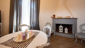 A cozy living room with a fireplace, a dining table with candles, and a window with curtains.