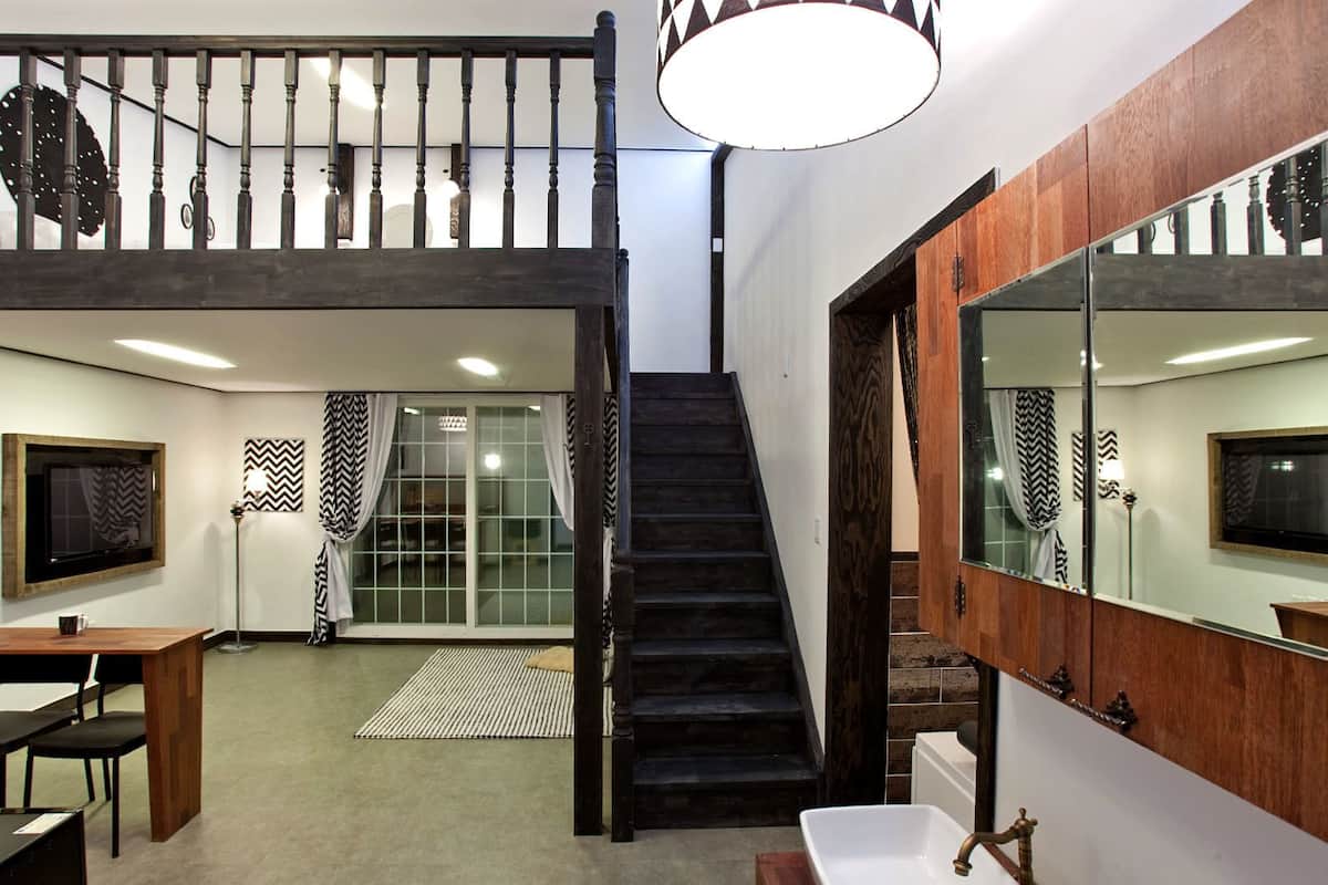 A modern interior with a staircase leading to a loft area, a large mirror, and a dining area with chairs.