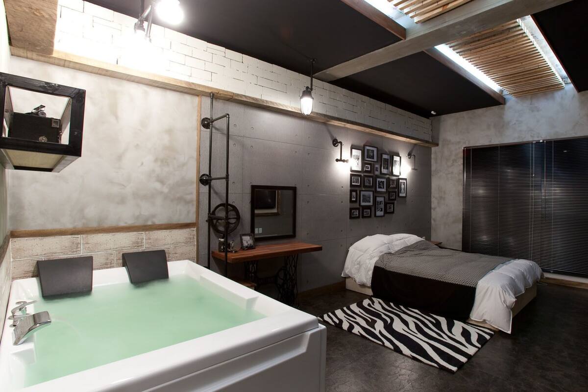 A modern bedroom with a large bathtub, a bed with a zebra-patterned rug, and a wall adorned with framed photos.