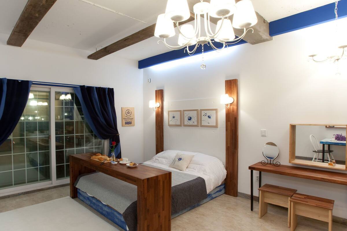A bedroom with a bed, bedside table, desk, chair, and a mirror.