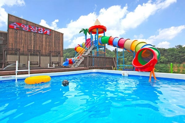 A swimming pool with a colorful water slide and a wooden building with signage. - Monopoly Pension (Gyeongju)
