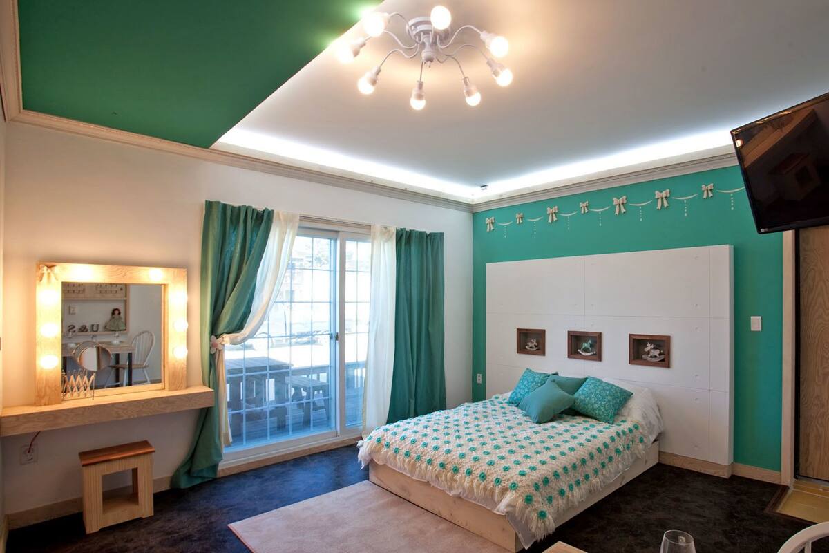A bedroom with a bed, a vanity with a mirror, a television, and a window with curtains.