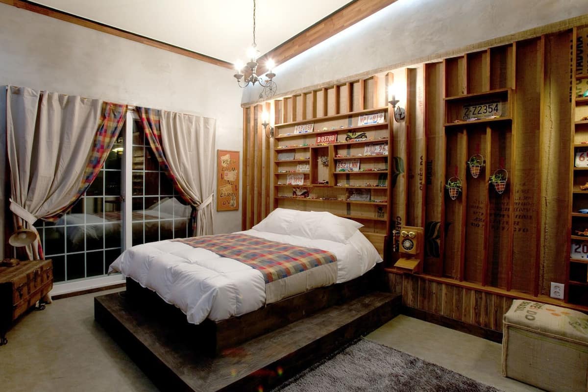 A bedroom with a bed, a window with curtains, a wooden bookshelf, and a vintage telephone.